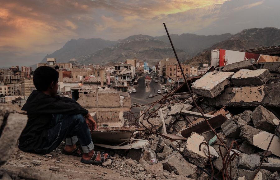 A child from Taiz City sits on the ruins of his ruined home beca